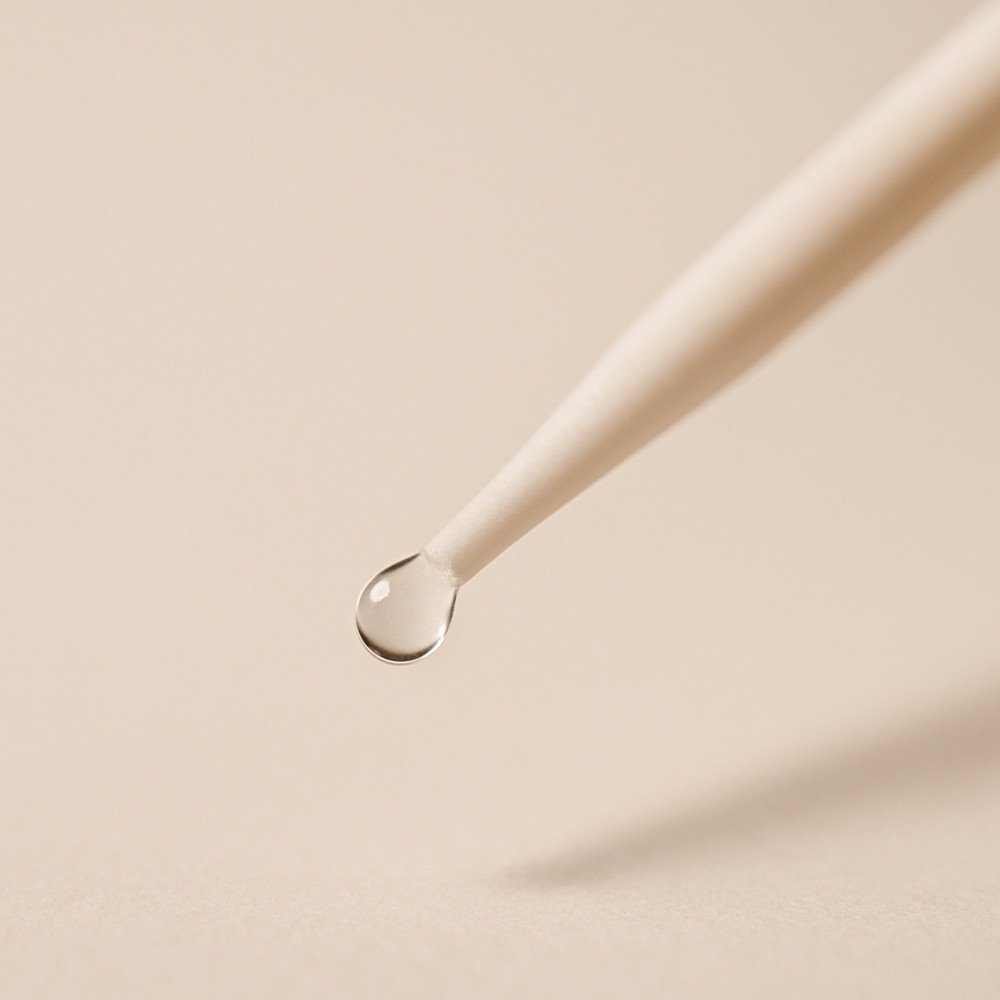 AI-generated editorial photograph of a small adhesive dot on an applicator wand